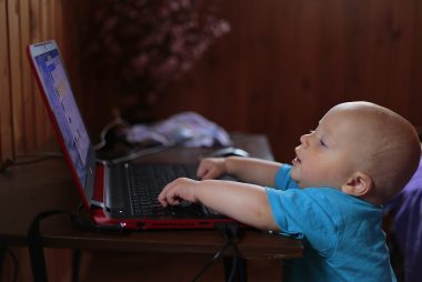 boy wearing blue t shirt using black laptop computer in a dim lighted scenario