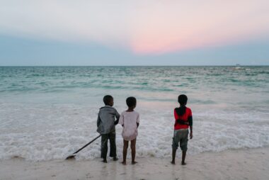 ethnic boys standing on seashore at sunset